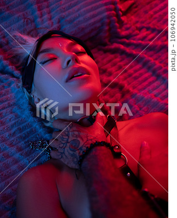 sexy BDSM girl with leather straps on the bed enjoys sex in orgasm with a man squeezing her neck in neon light sexy BDSM girl with leather straps on the bed enjoys sex in orgasm with a man squeezing her neck in neon light 106942050