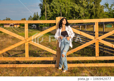 Beautiful young caucasian woman standing at the ranch gate. Beautiful young caucasian woman standing at the ranch gate. 106942077