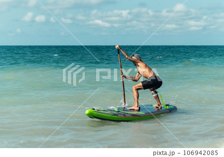 athletic wiry surfer guy swims with a paddle on a sapboard in the sea 106942085