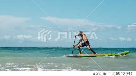athletic wiry surfer guy swims with a paddle on a sapboard in the sea athletic wiry surfer guy swims with a paddle on a sapboard in the sea 106942094
