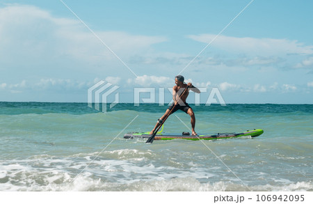 athletic wiry surfer guy swims with a paddle on a sapboard in the sea athletic wiry surfer guy swims with a paddle on a sapboard in the sea 106942095