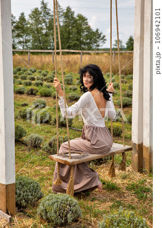 Beautiful young caucasian woman sitting on a wooden swing. 106942101