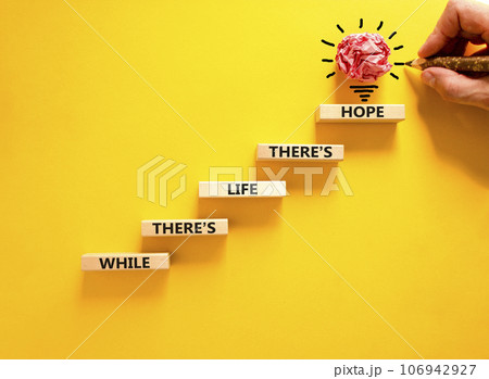 Life and hope symbol. Concept word While there is life there is hope on wooden block. Beautiful yellow table yellow background. Businessman hand. Business lifestyle life and hope concept. Copy space. 106942927