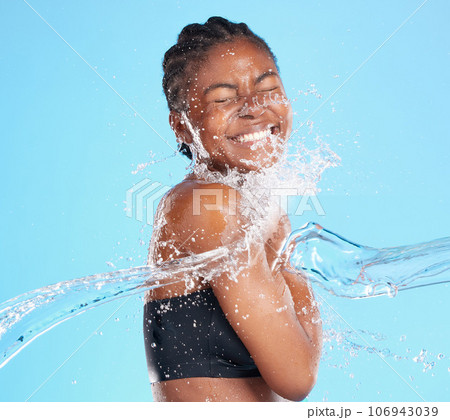 Her smile is sunshine. Shot of a beautiful young woman being splashed with water against a blue background. 106943039