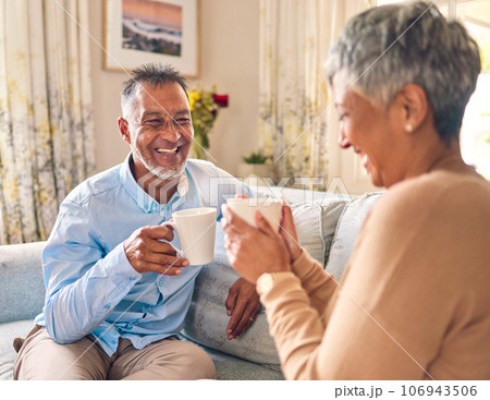 Coffee, laughing and a senior couple on a sofa in the home living room to relax while bonding in conversation. Smile, retirement or love with a mature married man and woman talking while drinking tea 106943506