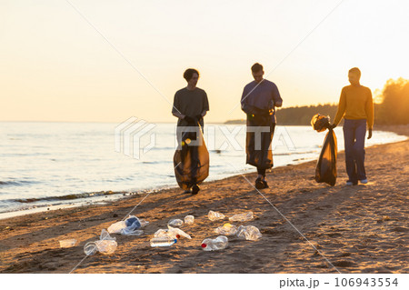 Earth day. Volunteers activists team collects garbage cleaning of beach coastal zone. Woman mans with trash in garbage bag on ocean shore. Environmental conservation coastal zone cleaning 106943554