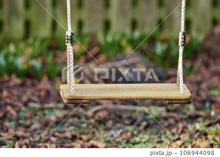 An empty wooden swing in a garden outside in the late afternoon with copyspace. A space to play in a backyard for active children wanting to have fun and play with copy space 106944098
