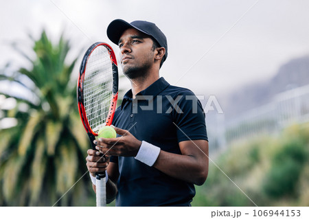 Young tennis player with racket standing outdoors 106944153