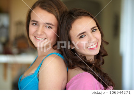 Happy sisters, portrait and standing back to back for family, friends or teens together at home. Face of female people, siblings and smile for friendship, relationship or young women in the house 106944271