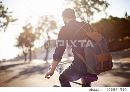 Bicycle, travel and back of man in street with lens flare for exercise, commute and cycling in morning. Transport, city and male cyclist on bike for eco friendly traveling, carbon neutral and journey Bicycle, travel and back of man in street with lens flare for exercise, commute and cycling in morning. Transport, city and male cyclist on bike for eco friendly traveling, carbon neutral and journey 106944516