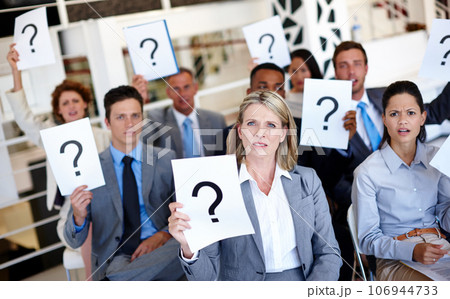 Stop leaving us in the dark. Shot of a group of businesspeople holding up signs with question marks on them during a work presentation. 106944733
