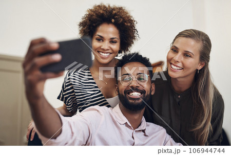 Group of office friends taking a happy selfie using a phone in business place. Cheerful, excited and joyful colleagues, work team and coworkers taking fun photos together. 106944744