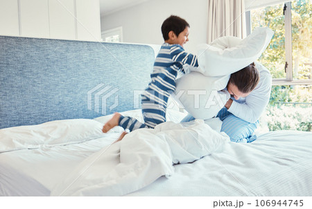 Playing, dad and son in pillow fight on bed, fun quality time and man bonding with child at home. Smile, happy and play, father and kid in bedroom with pillows, joy and happiness together on weekend. 106944745