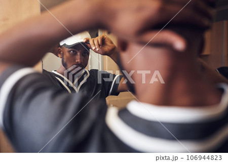 Baseball player, cap and face of sports man in a locker room getting ready and dressing in mirror. Behind an African athlete person with reflection and hat for sport competition, training or exercise 106944823