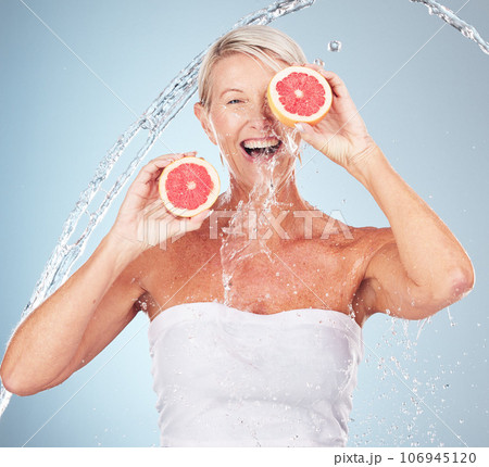 Woman, studio portrait and grapefruit with water splash, smile and happy for wellness by blue background. Senior model, organic citrus fruit and vitamin c for health, nutrition and self care process 106945120