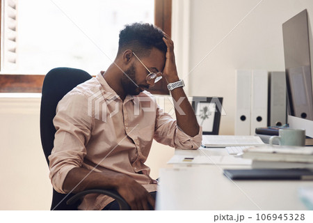 Facing a tough challenge in his workday. Shot of a young businessman looking tired while working in an office. 106945328