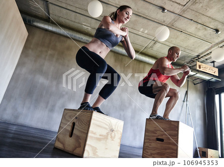 Gym, fitness and friends with jump box for training, workout and intense cardio on wall background. Jumping, exercise and people at a sports center for wellness, performance and endurance challenge 106945353