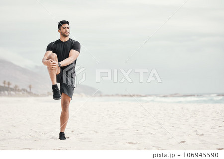 Stretch your day by starting it with a workout. a young man stretching on the beach. 106945590