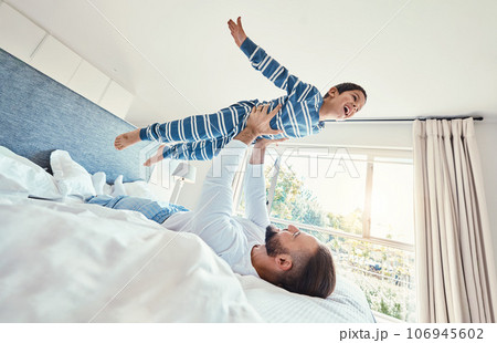 Father, son and dad playing with his child on a bed holding him having fun in a bedroom feeling happy, carefree and excited. Parent, kid and dad bonding with young boy in a house together 106945602