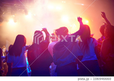 Crowd, people dancing at concert or music festival from back, neon lights and energy at live event. Dance, fun and group of excited fans in arena at rock band performance or audience at rave party. 106946660