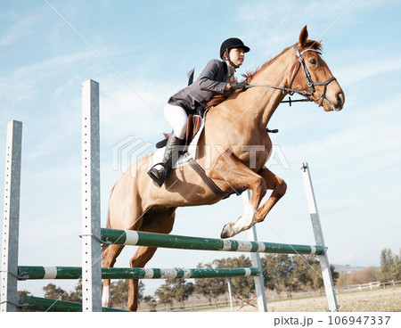 Over we go. Full length shot of a young female rider jumping over a hurdle on her horse. 106947337