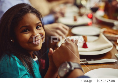 Portrait, meal and girl with her family, prayer and happiness with joy, home or religious. Face, young person or female child holding hands, praying and worship for blessing, food or social gathering 106947500