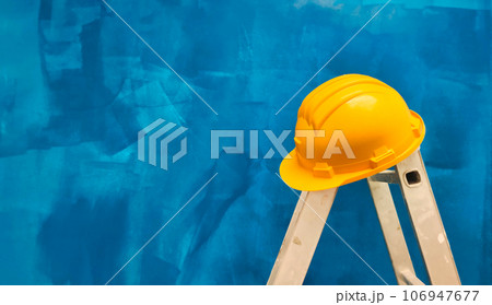 a ladder with a hard hat on a background of a blue wall a ladder with a hard hat on a background of a blue wall 106947677