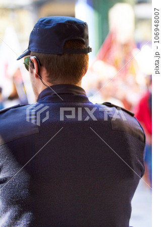 Keeping it legal. Rearview shot of a policeman keeping watch over a group of protesters. 106948007