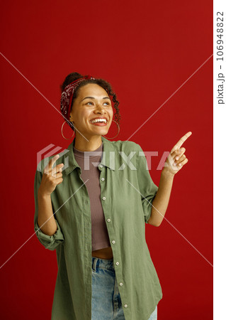 Positive woman is pointing finger at side with smile on red studio background. High quality photo 106948822
