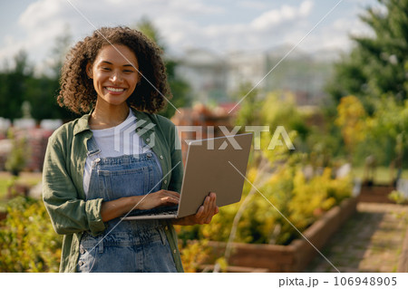 Woman gardener working on laptop while sitting on background of shop plants center 106948905
