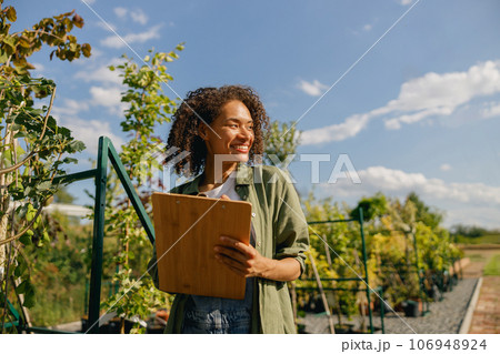 Cheerful woman gardener making notes in clipboard while standing in garden center 106948924