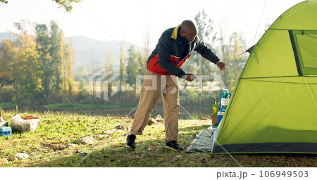 Camping, tent and black man setup in nature for shelter on outdoor holiday, vacation and adventure, Campsite, traveling and male person with hammer for pins for gear in woods, forest and countryside 106949503