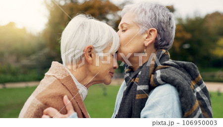 Senior woman kissing her friend on the forehead for affection, romance and bonding on outdoor date. Nature, commitment and elderly female couple in retirement with intimate moment in garden or park. 106950003