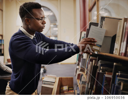 University, research and man in a library reading and learning on campus for knowledge and education in college. Smart, clever and young person in an academy with books on a shelf for an exam University, research and man in a library reading and learning on campus for knowledge and education in college. Smart, clever and young person in an academy with books on a shelf for an exam 106950036