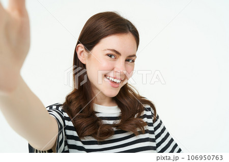 Portrait of beautiful young woman, 25 years old, holds smartphone, takes selfie, posing for a photo, standing over white background 106950763