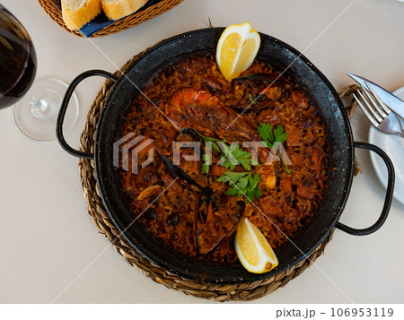Fresh hot paella with seafood in cast-iron pan. There is cast-iron baking dish with hot lunch on stand for hot Fresh hot paella with seafood in cast-iron pan. There is cast-iron baking dish with hot lunch on stand for hot 106953119