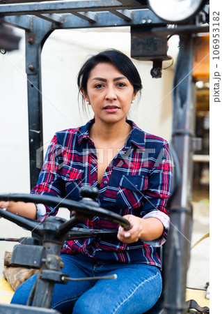 Confident hispanic woman sits behind the wheel of a forklift truck. 106953182