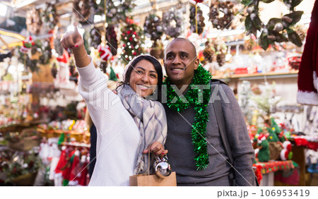 Married couple looking for decorations on Christmas street market while shopping Married couple looking for decorations on Christmas street market while shopping 106953419