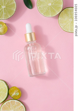 A glass dropper bottle without label decorated with slices of lime and kumquat on a pink background. Mockup scene for advertising with natural extract and natural essential 106954605