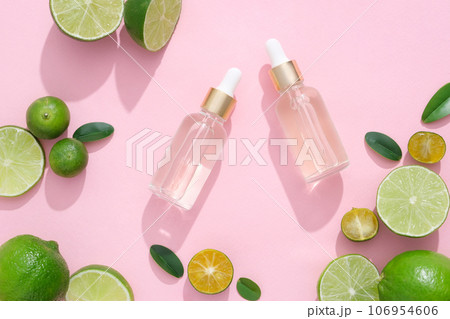 Scene for advertising cosmetic product with ingredient from natural. Kumquat and lime slices decorated with glass dropper bottles on a pink background. Top view, space for design 106954606