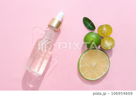 On a pink background, a dropper bottle is open decorated with lime slice and halves of kumquat. Scene for advertising product with natural ingredient. Minimalist concept 106954609