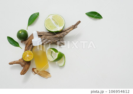 Natural vitamin C skincare product with fresh lime slices decorated with green leaves and dry twig on white background. Minimalist concept for advertising. Copy space 106954612