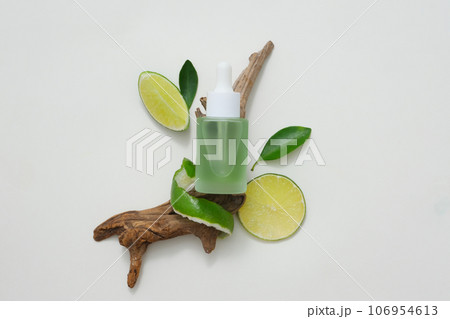Natural vitamin C skincare product with fresh lime slices decorated with green leaves and dry twig on white background. Mockup scene for advertising and space for design 106954613