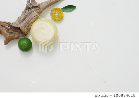 Top view of yellow jar filled with cream texture, decorated with slices of kumquat, dry twig and green leaves on a white background. Empty space for mockup bottle display 106954619