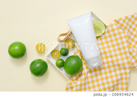A white plastic tube container moisturizer cream or facial cleanser with ingredient from natural extract, decorated with lime and kumquat slices on beige background 106954624