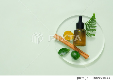 Natural ingredients - cinnamon, kumquat and green leaves decorated with amber dropper bottle on transparent podium. Blank space for presentation product Natural ingredients - cinnamon, kumquat and green leaves decorated with amber dropper bottle on transparent podium. Blank space for presentation product 106954633