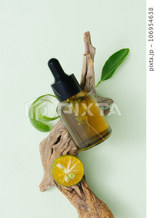 Concept of natural cosmetics with lime extract. A dropper bottle unbranded displayed on dry twig with kumquat slice and leaf. Top view, minimalist concept 106954638