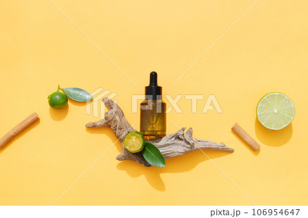 An amber serum bottle displayed on orange background with some natural ingredients: lime, kumquat and cinnamon stick. Their essential oils help improve mood and boost the brain 106954647