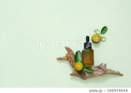 A product bottle mockup displayed with dry twig, kumquat slices and leaves on green background. Copy space for cosmetics, business branding and product presentation 106954648