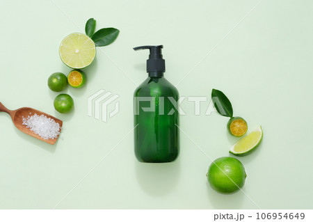 A pump bottle container shampoo or shower gel decorated with slices of lime and kumquat, green leaves and wooden tray of bath salt on green pastel background 106954649